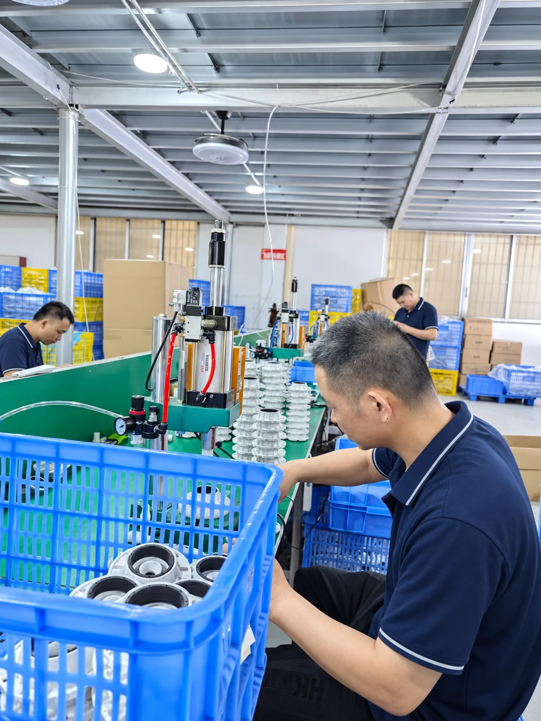Operator working at a pneumatic press beside rows of metal housings on a green workbench
