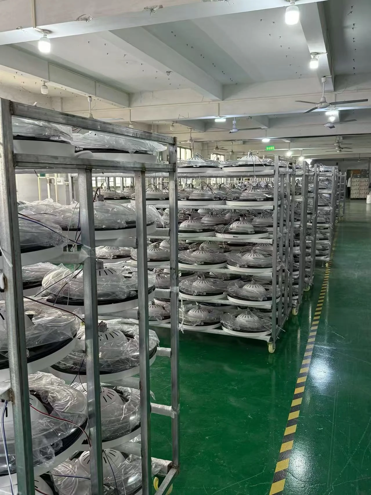 Round lighting units with protective covers on wheeled racks beside a marked factory aisle